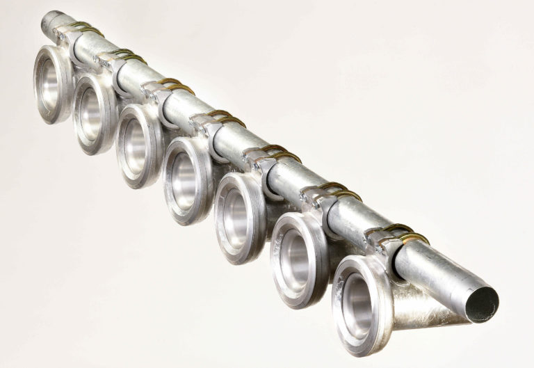 Ein Arbeiter befestigt acht gleichmäßig verteilte runde Ersatzteilflansche an einem Metallrohr vor einem neutralen Hintergrund.