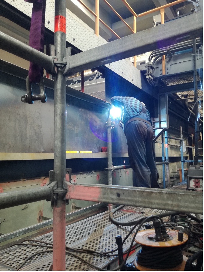 Ein Arbeiter in Schutzkleidung schweißt auf einer Baustelle mithilfe von Filtertechnik in der Nähe von Gerüsten und Geräten Metall.