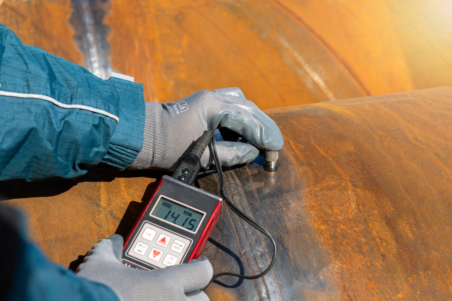 Eine Person misst die Dicke der Rostoberfläche mit einem Ultraschallgerät; Anzeige: 14,15 mm.